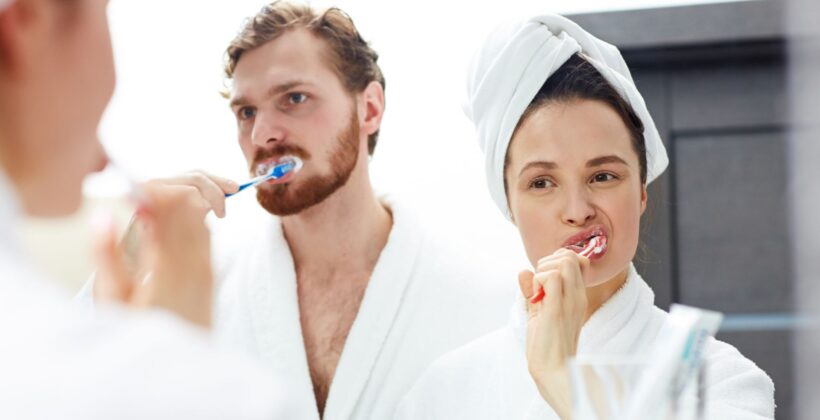 Couple looking into the mirror while brushing teeth - oral hygiene habits - Midland Bay Dental.